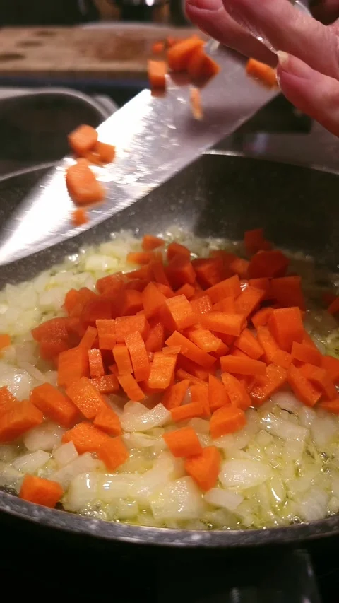 Adding chopped carrots to frying pan. 動画素材 346068381