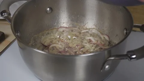 Adding chopped champignons to toasted onions in a metal saucepan Stock Footage 142776939