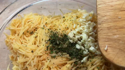 Adding chopped garlic into a bowl of grated potato. POV cooking hash browns at Stock-Footage 260273366