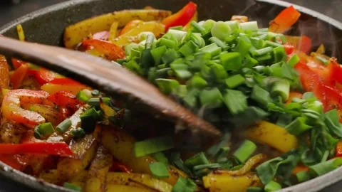 Adding chopped green onion to potatoes frying in a pan Stock Footage 315703651