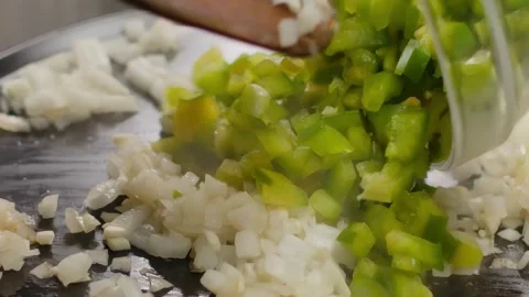 Adding chopped green pepper to frying onions in a pan Stock Footage 315703131