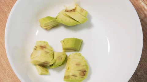 Adding chopped slices of raw avocado in a white bowl close-up, stop motion Stock Footage 126123143