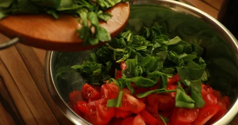 Adding chopped spinach to a bowl of tomatoes Video stock 244072890
