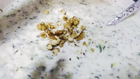 Adding chopped walnuts to traditional Persian yogurt and cucumber dish Stock Footage 345144482