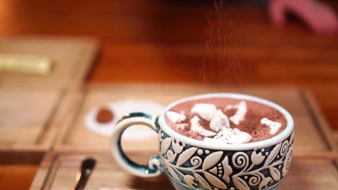 Adding cinnamon on top of marshmallow cacao in cute cappuccino coffee cup in Stock Footage 104414927