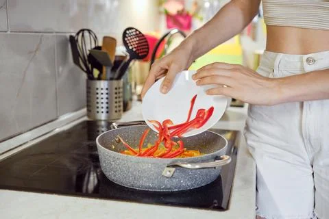 Adding colorful chopped bell peppers into a frying pan in a modern kitchen 库存照片