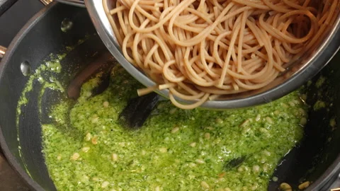 Adding cooked spaghetti to pesto in order to make pesto pasta. Italian food.. Video stock 302020633