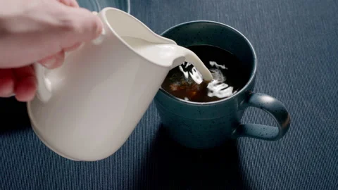 Adding cream to a blue cup on a table. Milk coffee. Slow motion. Видео 144416014