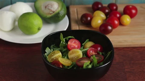 Adding diced avocado in to bowl with salad arugula and cherry tomatoes Stock Footage