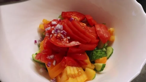Adding diced red onion into white bowl with fresh summer vegetable salad Stockbeeldmateriaal 344877068