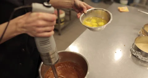 Adding the eggs to the bowl while the immersion blender is running. Stock Footage 256408758