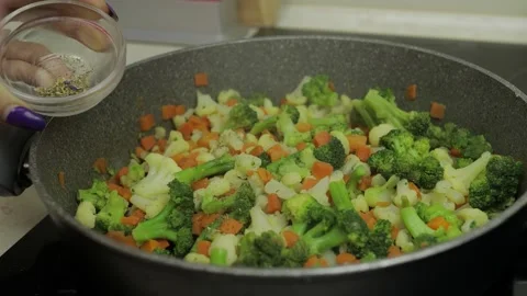 Adding flavoring to vegetables on frying pan. Carrots, cauliflower, broccoli Vidéo 130314820