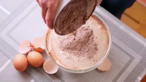 Adding flour and cocoa to beaten eggs - making dough for baking Stock Footage 186456499