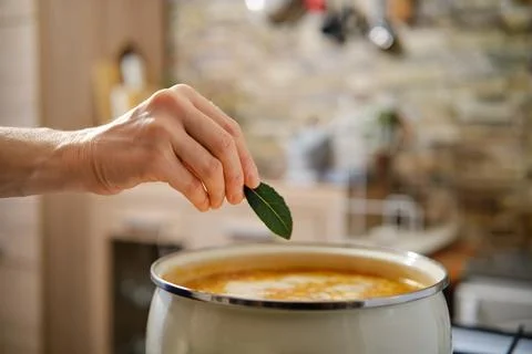 Adding fresh bay leaf to a simmering pot of soup in a cozy kitchen during t.. Foto stock