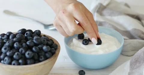 Adding fresh blueberries to yogurt. Stock Footage 249593856