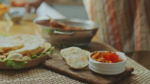 Adding Fresh Coriander to Indian Dish Served with Flatbread on Wooden Board Stock Footage 303021799
