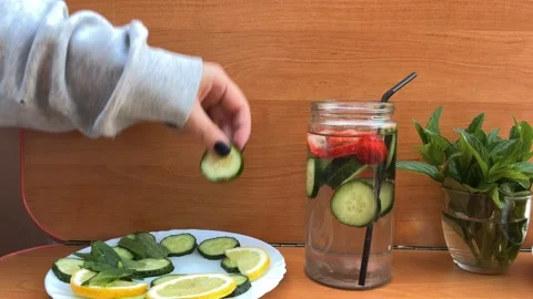 Adding Fresh Cucumber Slices into Glass Jar with Detox Water Stock Footage 335023907