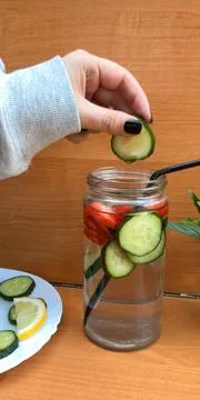 Adding Fresh Cucumber Slices into Glass Jar with Detox Water Stock Photos