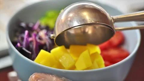Adding fresh mango cubes to healthy poke bowl with metal scoop. Stock Footage 339396792