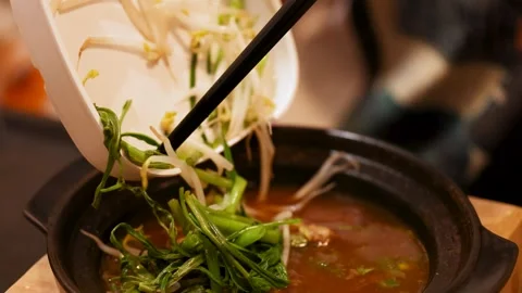 Adding Fresh Vegetables to Traditional Thai Beef Soup Hot Pot Stock Footage 345462990
