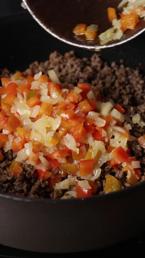 Adding Fried Diced Onion and Red Bell Pepper to Ground Beef in Pan Front View Видео 336568096