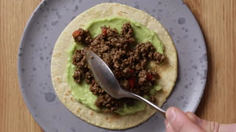 Adding Fried Ground Beef to Tortilla with Guacamole Close Up Top View Видео 336577549