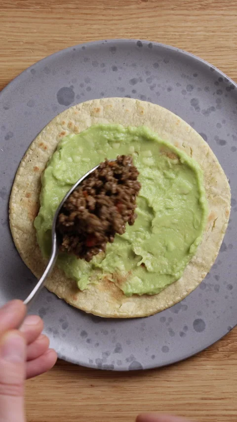 Adding Fried Ground Beef to Tortilla with Guacamole Vertical Top View Vidéo 336577872