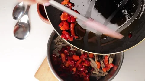 Adding fried red bell pepper into pot with cooked beef strips using spatula, top Stock Footage 317107754