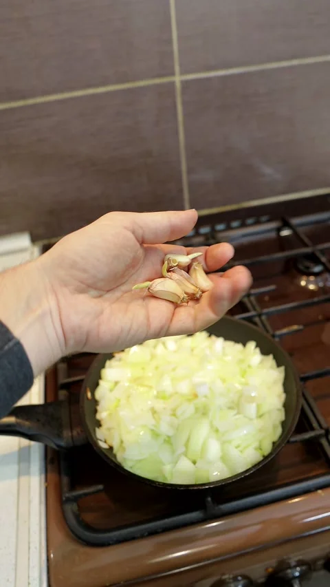 Adding garlic to fried onions in a frying pan, vertical video Stock Footage 169027537