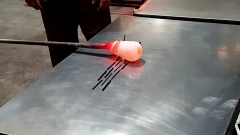 Adding glass colour stick over melted glass blowing process rolling on table Stock Footage 249819899
