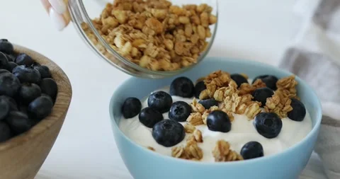 Adding granola to a bowl of yogurt and blueberries Stock Footage 249593742
