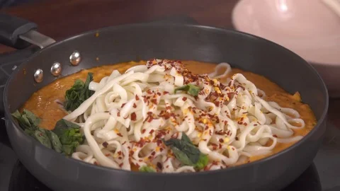 Adding green leaves and mixing  Pasta in Red Bell Pepper Sauce Stockbeeldmateriaal 79061421