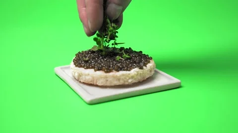 Adding greens on top of freshly made Caviar sandwich on a green background in 4K Stock Footage 149609412