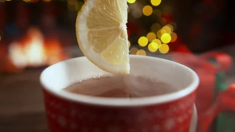 Adding Half a Slice of Lemon to Tea Steaming in Red Cup by the Fireplace Stock Footage 208932173