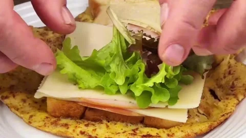 Adding ham cheese and lettuce to an egg omelette sandwich for a healthy meal Stock Footage 324943398