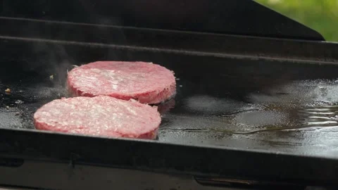 Adding hamburger patties to flat top grill Stock Footage 310253744