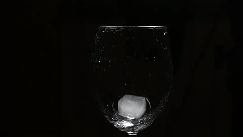Adding ice cubes into glass against dark background Видео 166284635