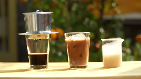 Adding Ice Cubes to Traditional Vietnamese Milk Coffee in Sunlight. Видео 333590422