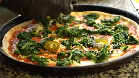 Adding jalapenos on top of a fresh pizza with spinach before baking Stock Footage 117415641