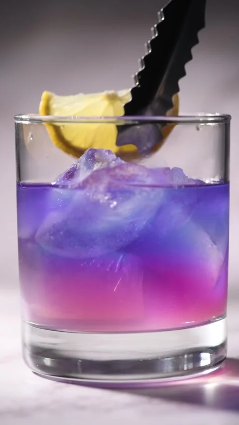 Adding lemon slice to butterfly pea tea with ice in low glass Stock Footage 337844221