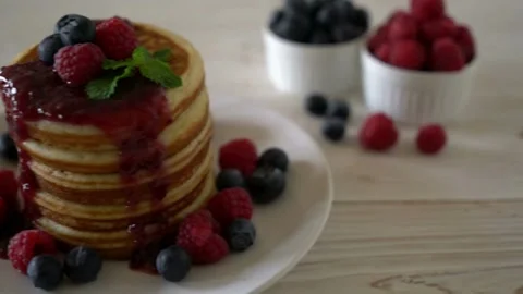 Adding maple syrup and fresh mix berries to pancakes. Stock-Footage 336589360