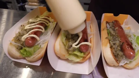 Adding mayonnaise ketchup and mustard on gourmet hot dogs in a fast food kitchen Stock Footage 324711120