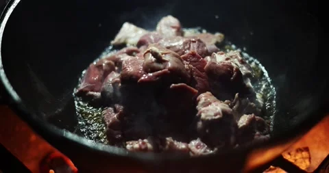Adding meat to fat in a hot cauldron while cooking pilaf.	 Video stock 168181105