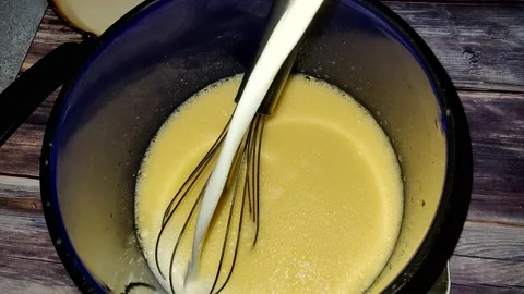 Adding milk to beaten eggs in a blue saucepan.  Cooking pancakes Stock Footage 232945775