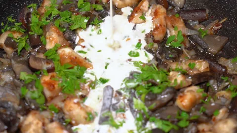 Adding milk cream to fried mushrooms in a hot pan at the home kitchen. Stock Footage 248228885