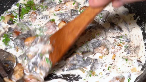 Adding milk cream to fried mushrooms in a hot pan at the home kitchen. Stock Footage 248228891