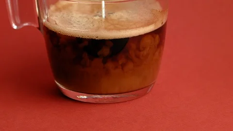 Adding milk to glass cup of coffee, red background Stock Footage 85591848