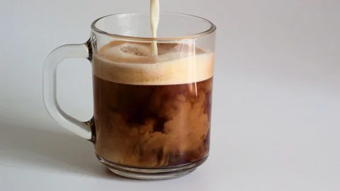 Adding milk to a glass mug with fresh fragrant black coffee Stock Footage 105052797