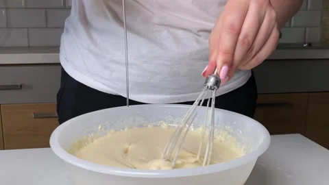 Adding oil and mixing pancake batter with whisk in white bowl. close-up of Stock Footage 316472578