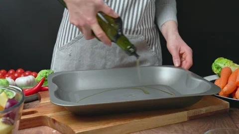 Adding oil into an oven pan from a bottle and brushing with a brush in 4k. Stock Footage 145114565